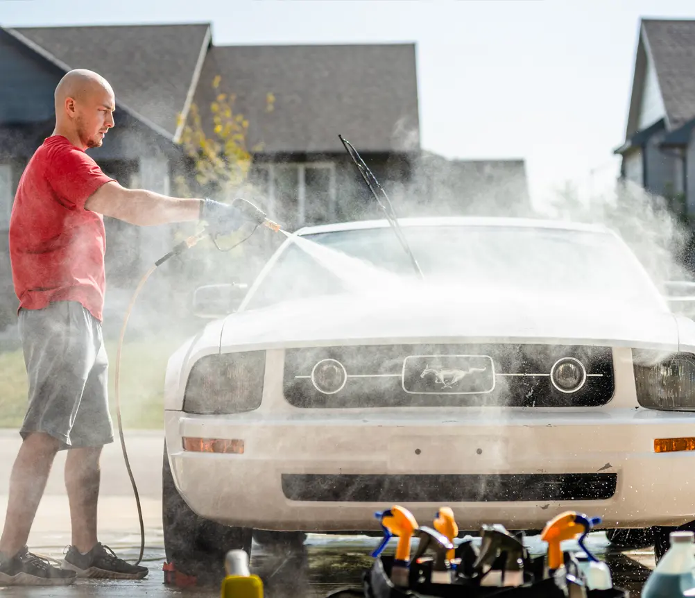 Detailer pressure washing a white Ford Mustang