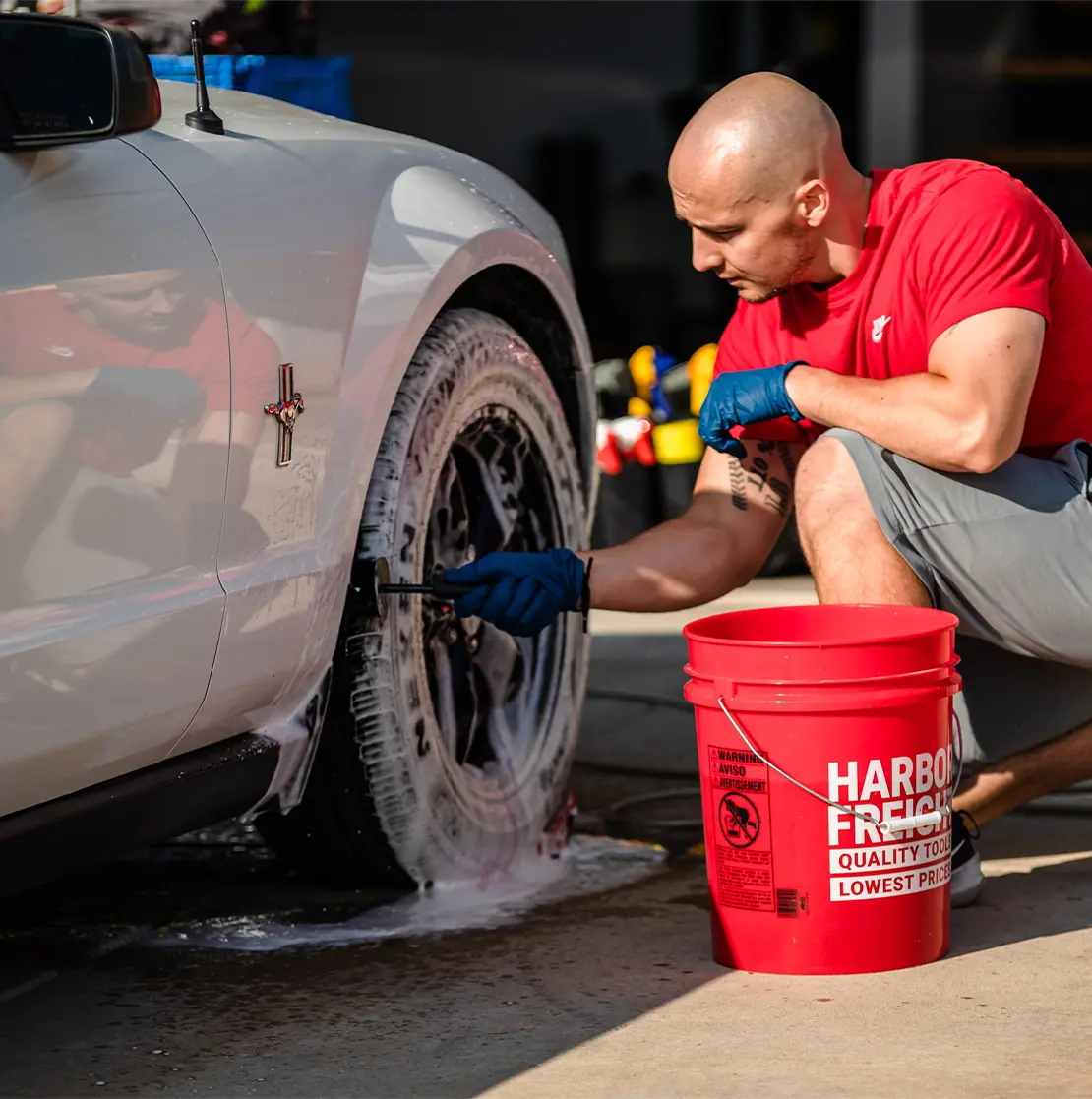 Detailer cleaning the wheel of a white Ford Mustang